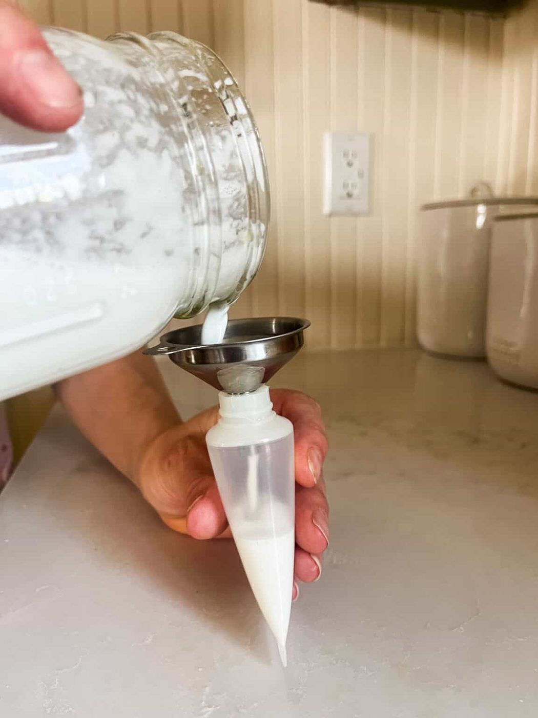 Pouring homemade tallow lotion into a squeeze bottle with a small funnel.