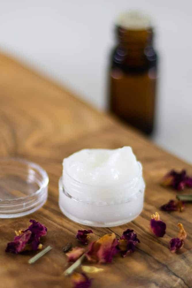 homemade eye cream on wooden board with essential oil bottle in background