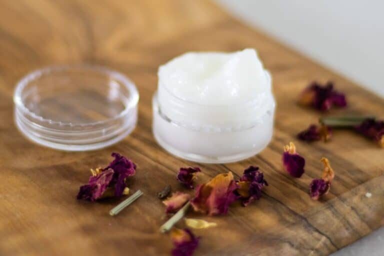 coconut oil eye cream in small container on wooden board with rose petals around it