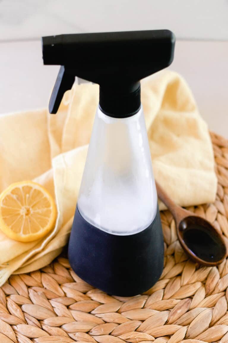 A bottle of homemade wasp spray with spoon and lemon nearby.