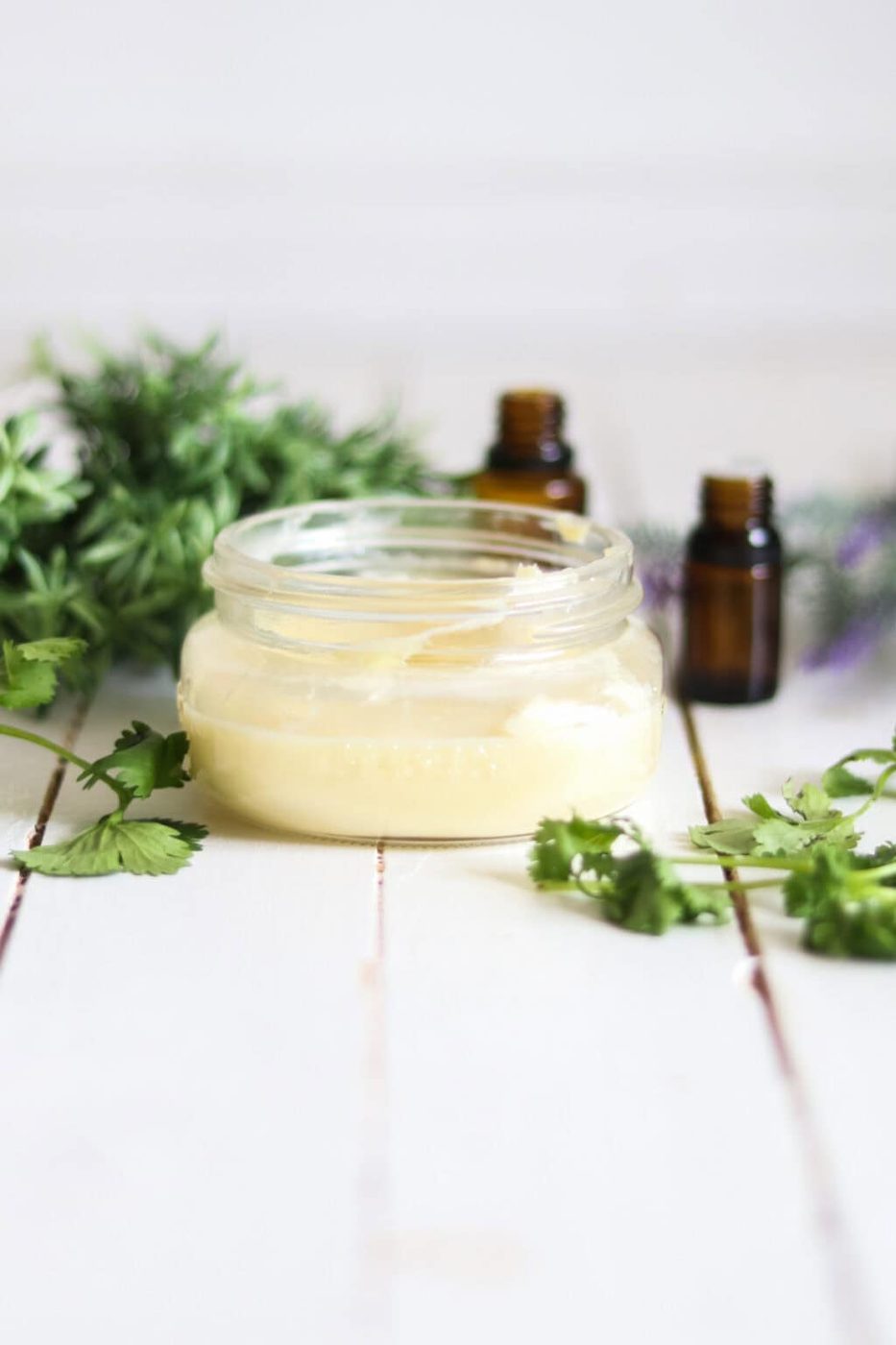 Homemade whipped body butter with lavender sprigs and essential oil bottles.