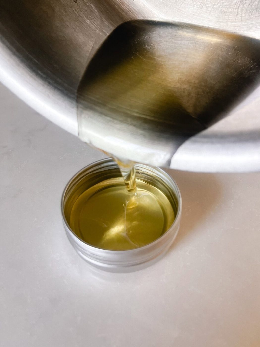 Pouring melted wood balm into a metal tin.