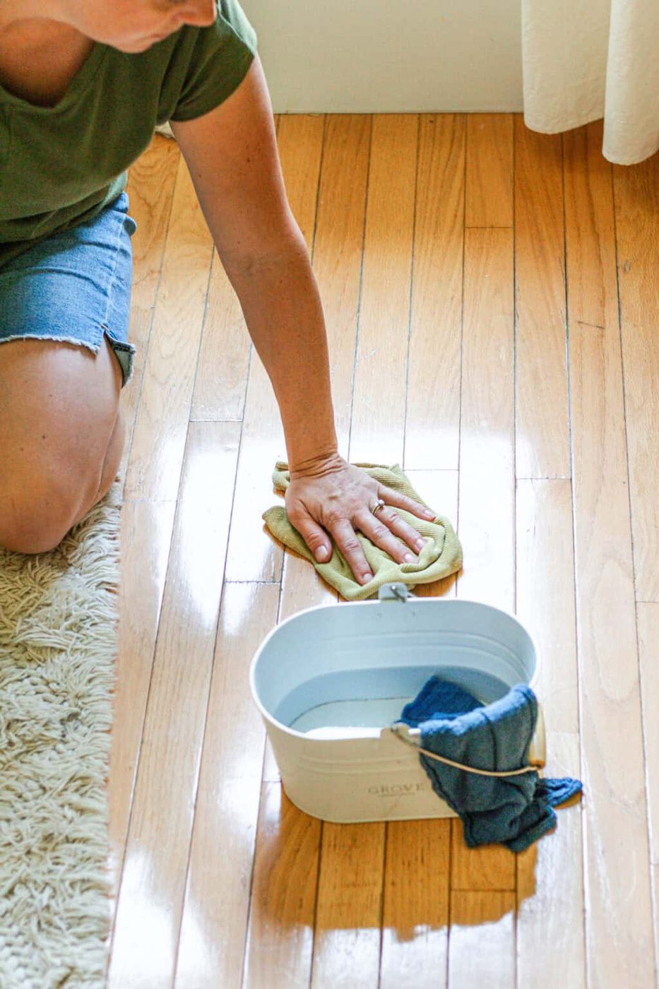 Wiping wood floors with a rag and a bucket of wood cleaner.
