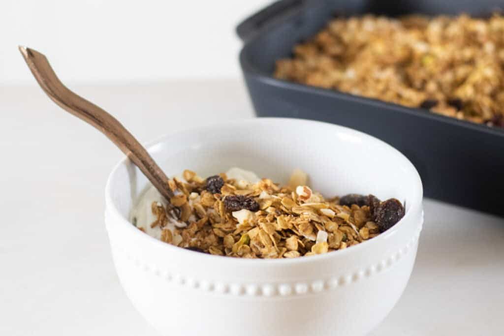 A white bowl of honey granola with a spoon sticking out of it.