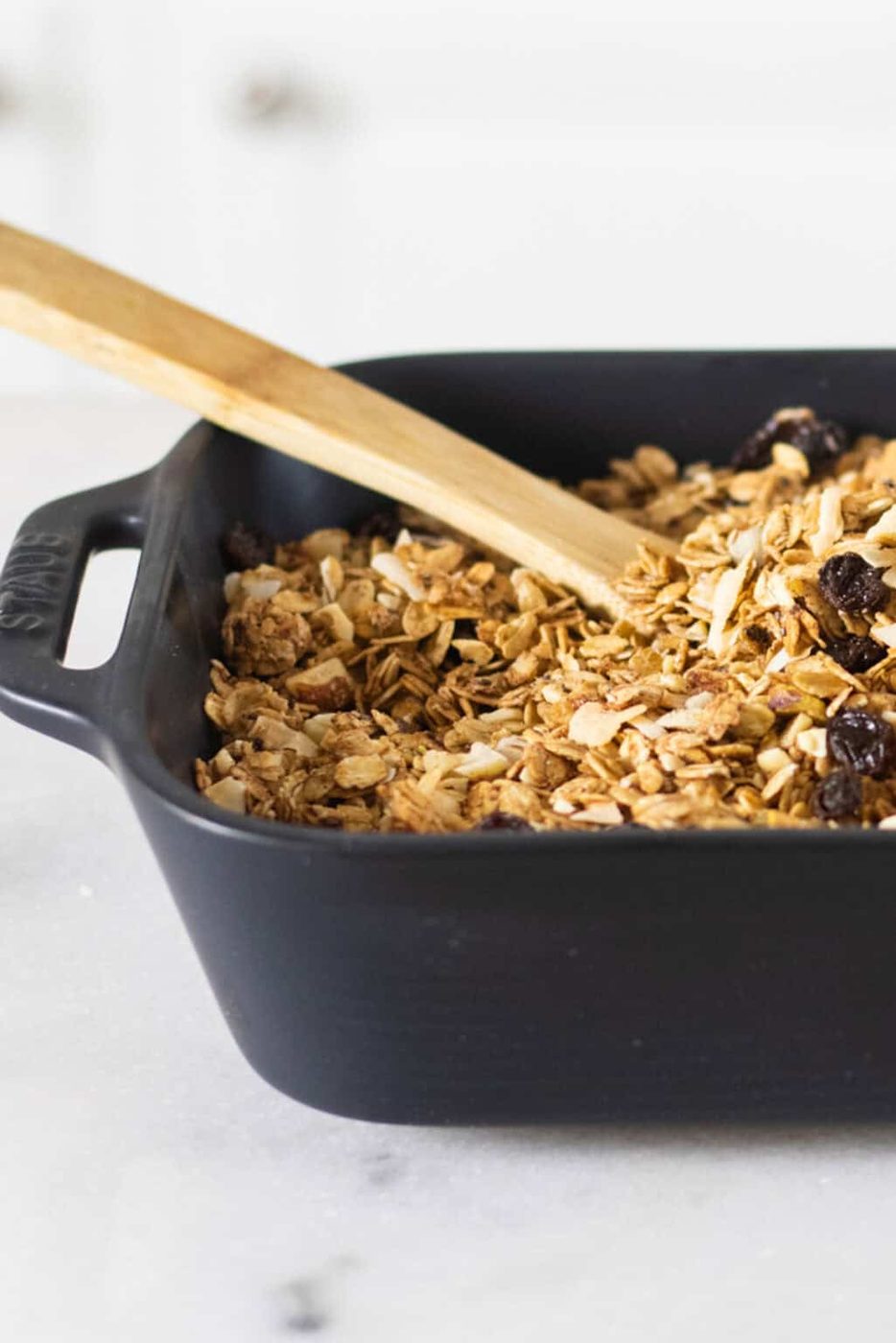 A baking dish filled with honey granola with a wooden spoon in it.