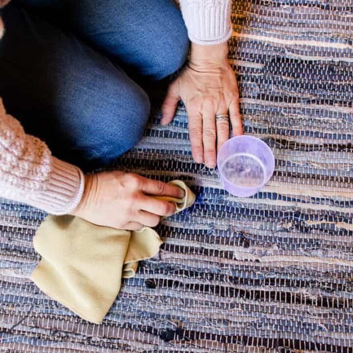 Spot treating a blue braided rug with a little laundry detergent and a clean cloth.