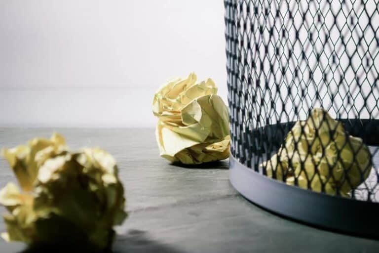A trashcan with crumpled papers in and around it.