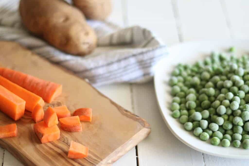 Potatoes, sliced carrots, and peas on wooden table.