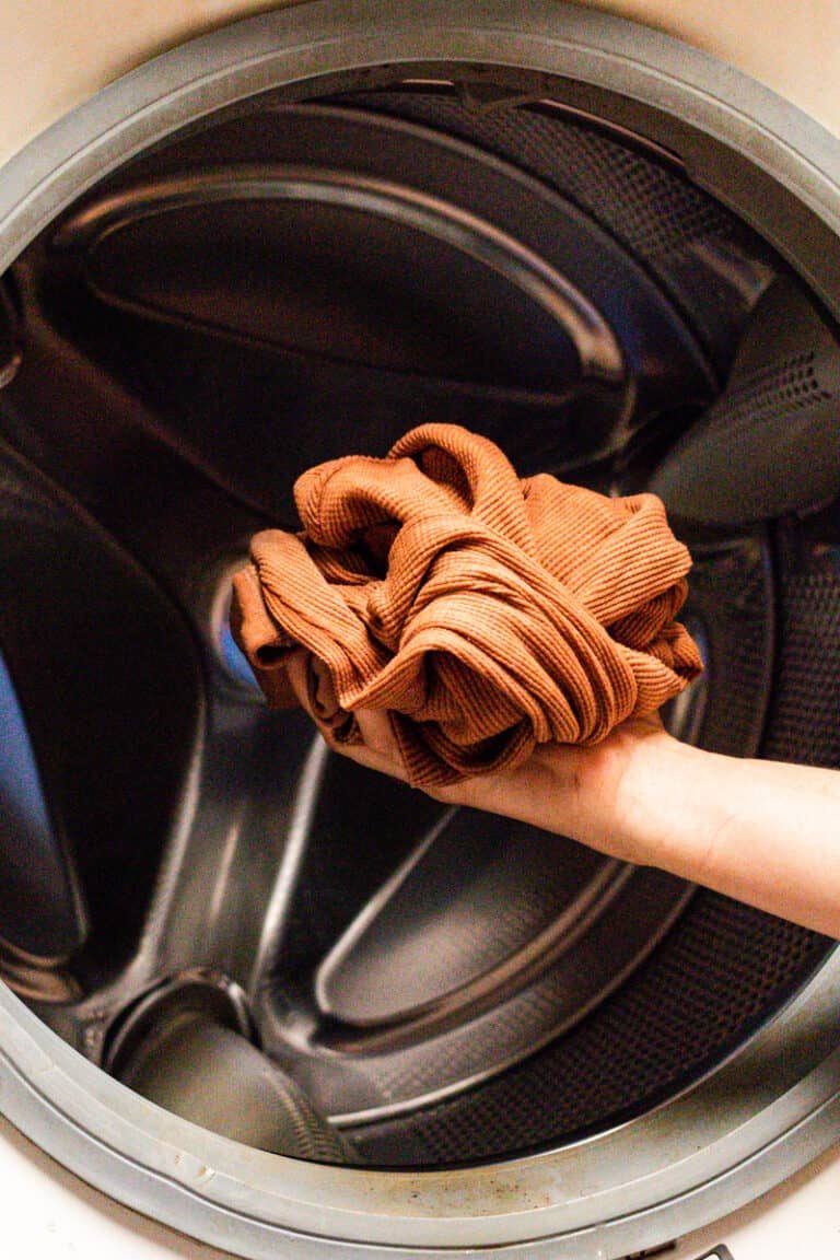 Putting an item of clothing into the washer.