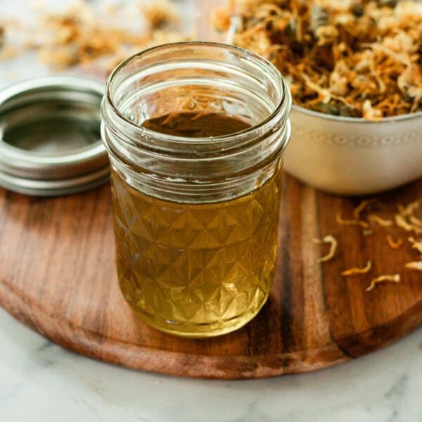 A jar of calendula oil and a bowl of dried calendula flowers.