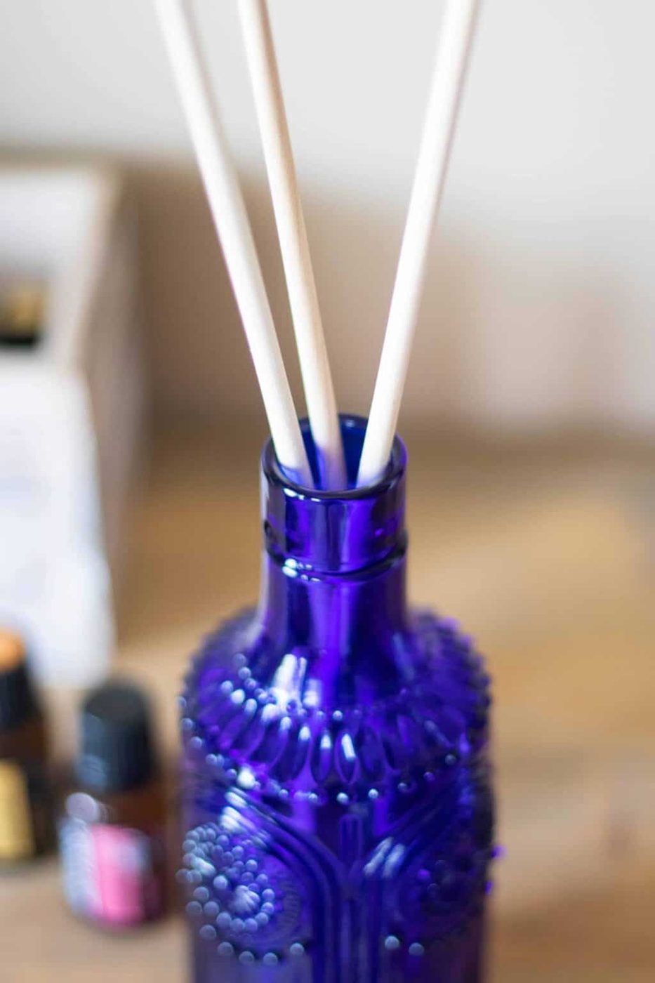 Blue essential oil reed diffuser on table with essential oil bottles in background.
