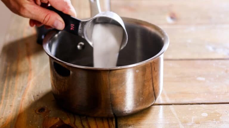 Pouring 1/4 cup sugar into saucepan of water.