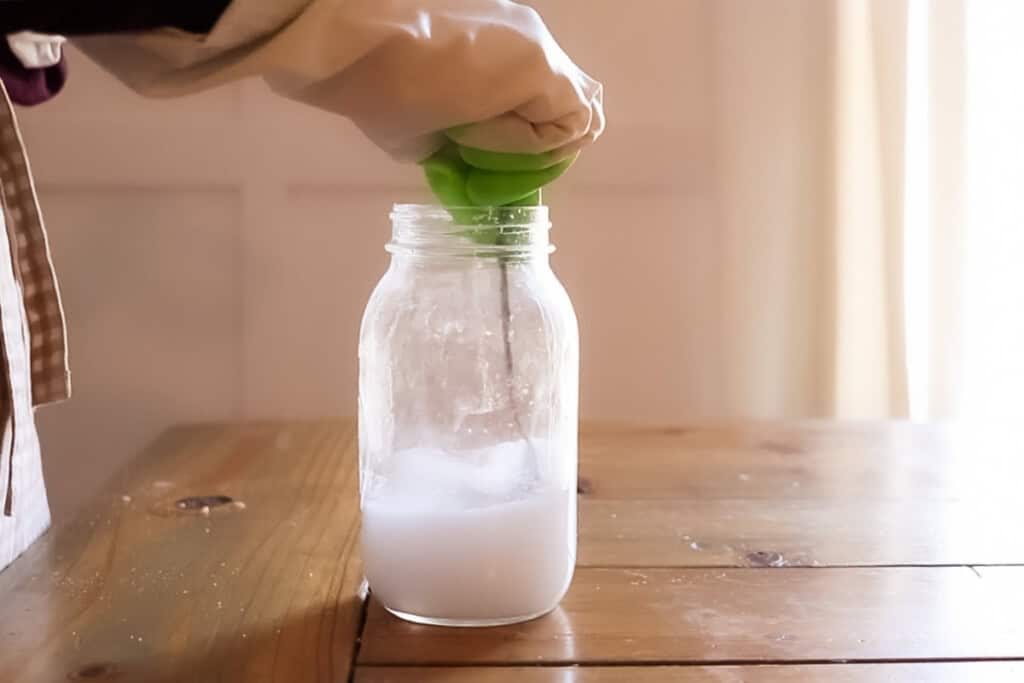 Stirring lye and water in a mason jar with gloves on.