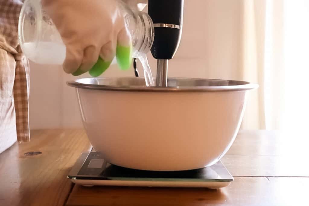 Pouring lye/water mixture into the mixing bowl while mixing with an immersion blender.
