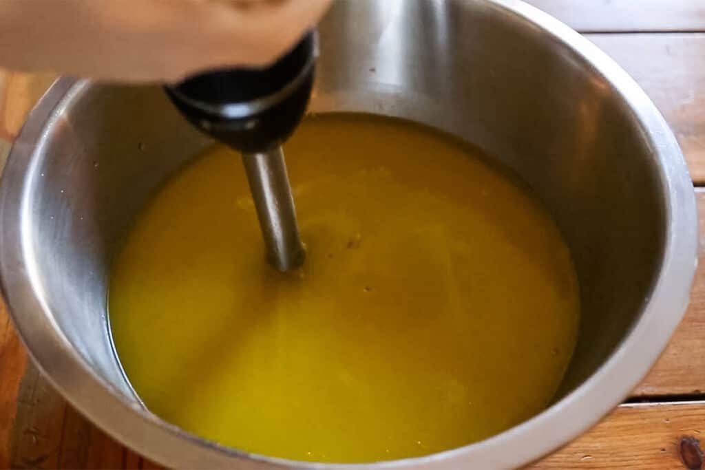 Blending soap mixture with an immersion blender in a mixing bowl.