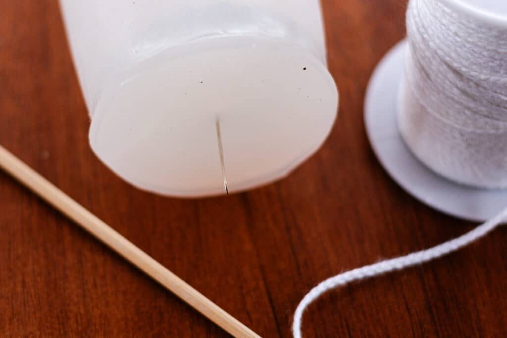 Poking the bottom of the silicone mold with a needle to thread the wick through.