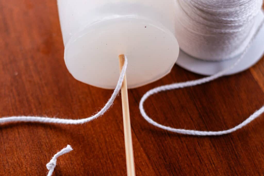 Feeding the candle wick through the small hole made with the needle.