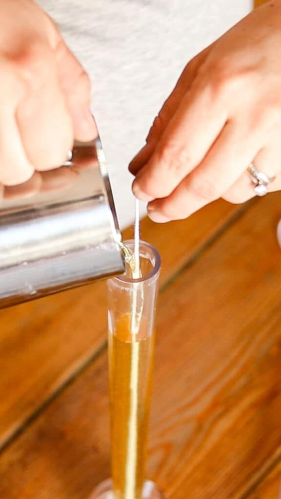 Pouring the melted wax into the candlestick mold while holding the wick taunt.