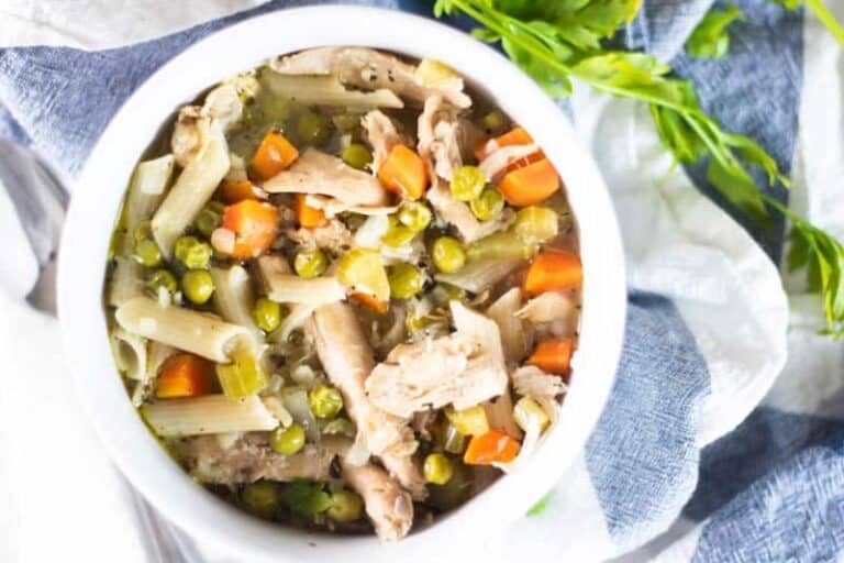 Turkey noodle soup in bowl sitting on blue and white towel with parsley sprigs.