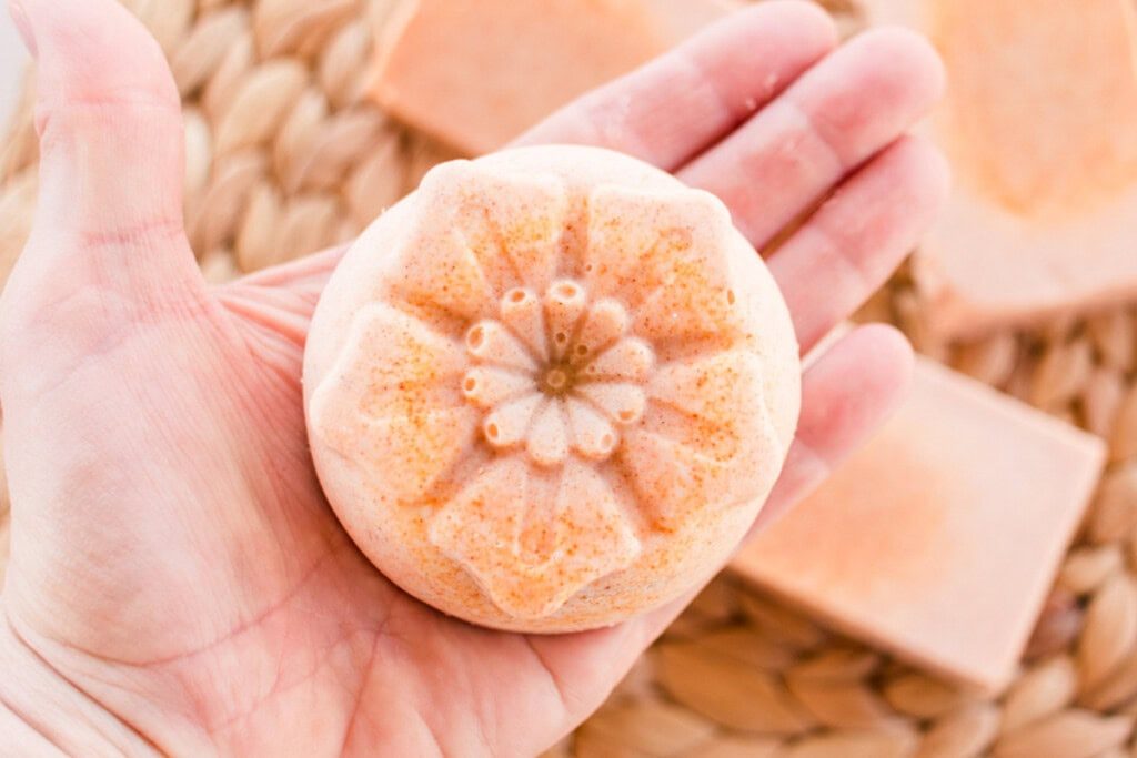 Holding a flower-shaped bar of orange soap in the palm of a hand.