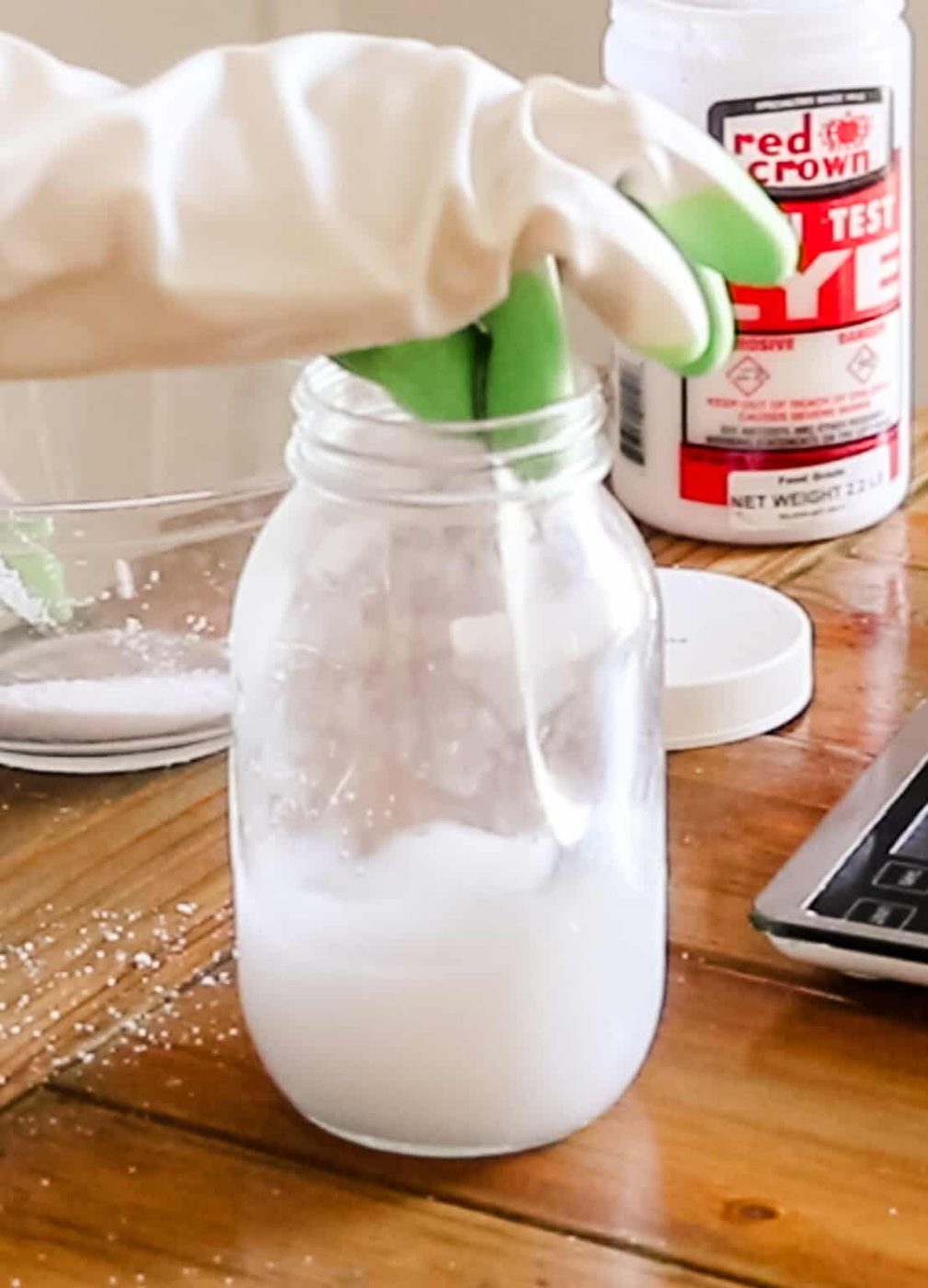 Stirring lye and water in a glass jar with gloved hands.