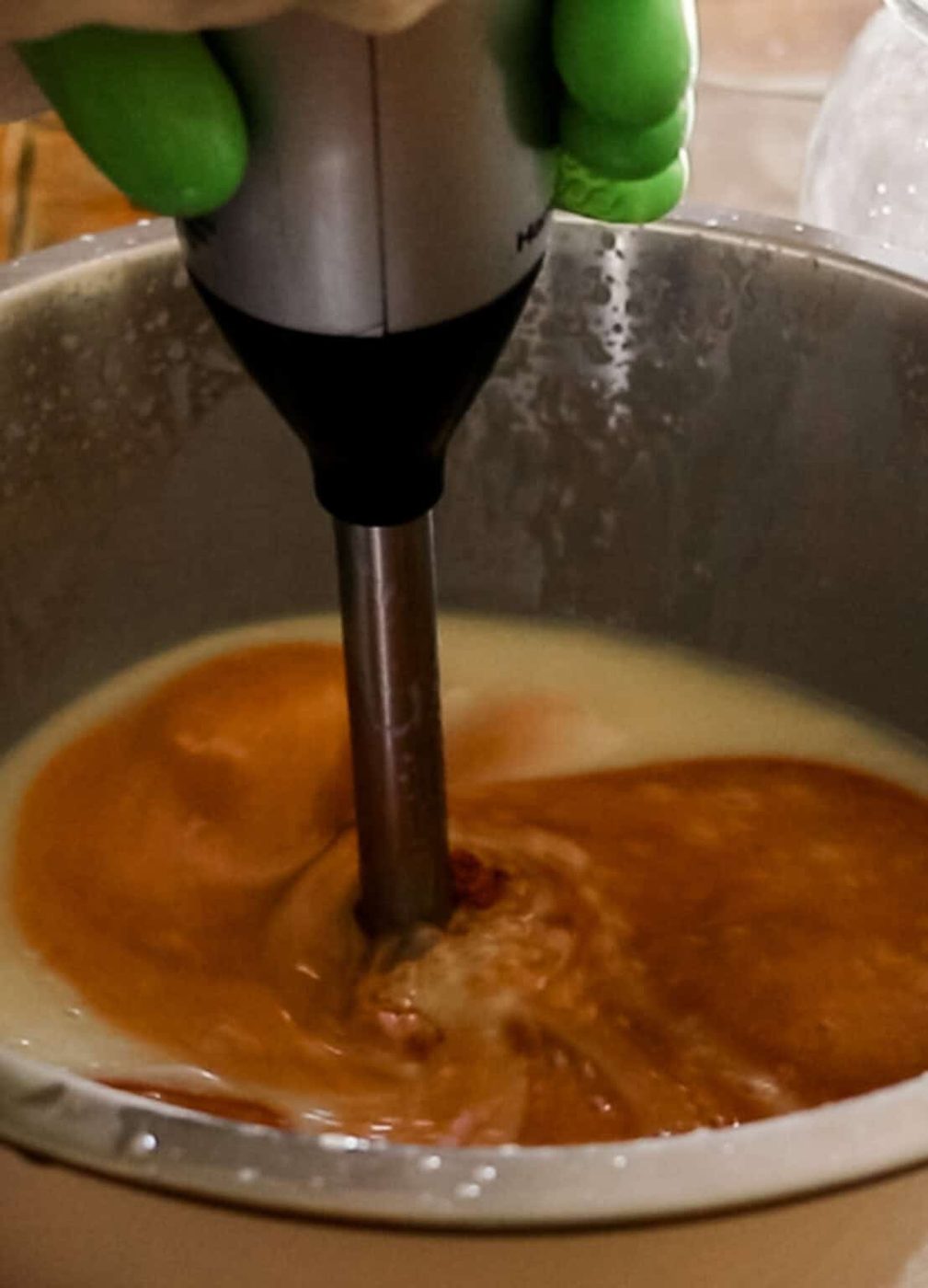 Mixing turmeric into the soap ingredients with an immersion blender.