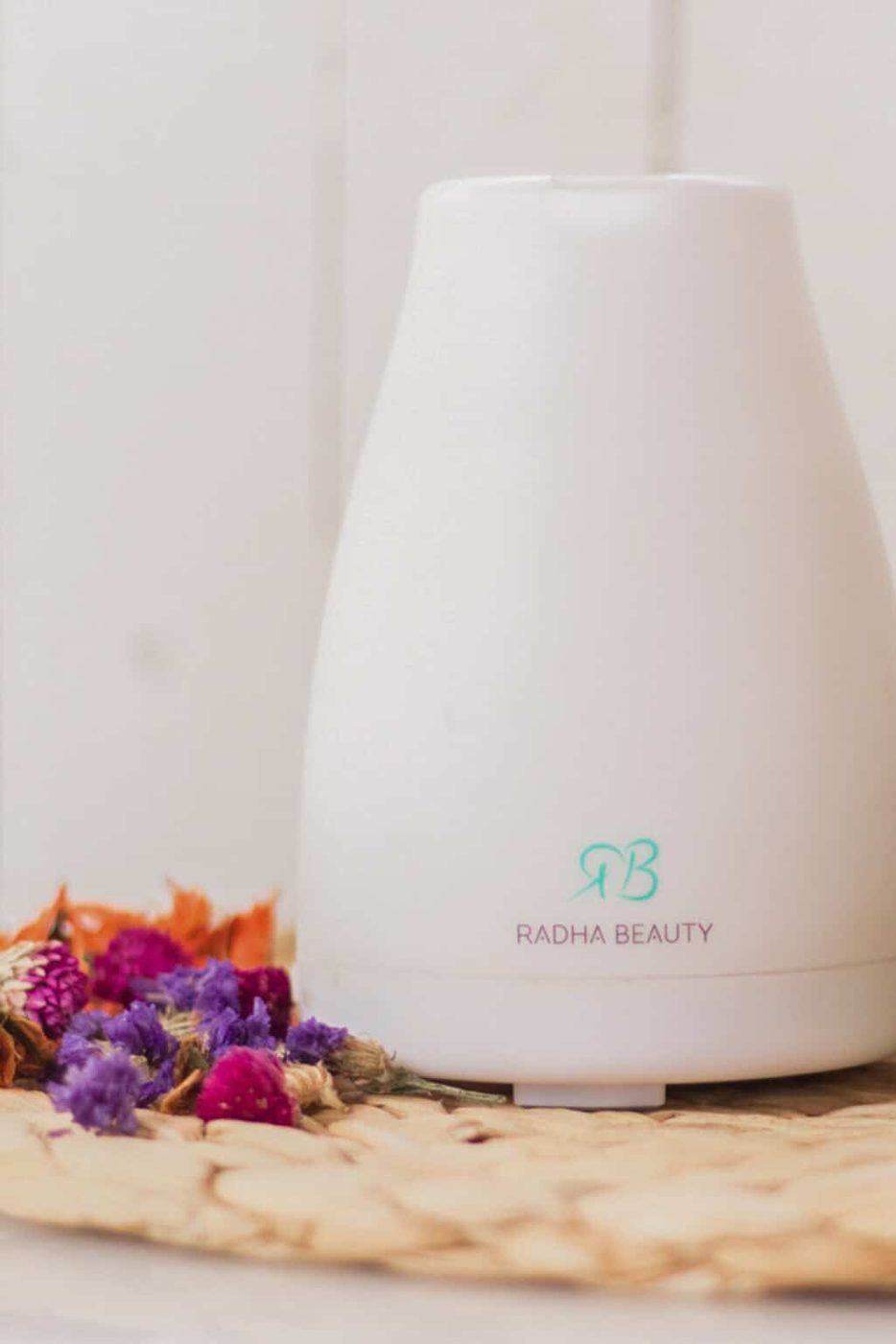 An essential oil diffuser on a wicker placemat with fresh flowers.