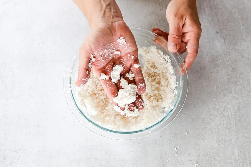 Pressing the mixture together into clumps, signaling that it is ready to be pressed into molds.