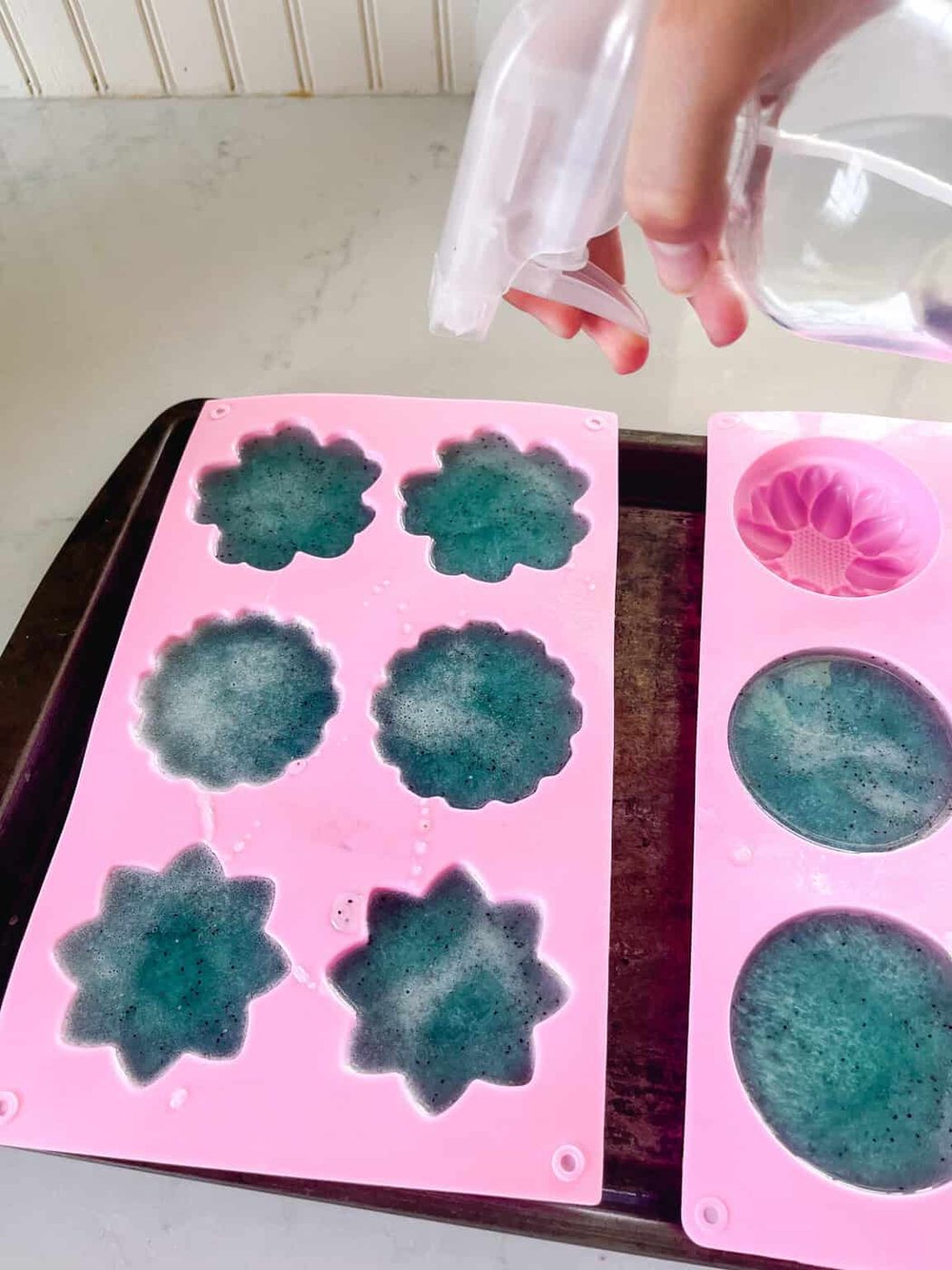 Spraying the top of the melted soap base with rubbing alcohol in its silicone molds.