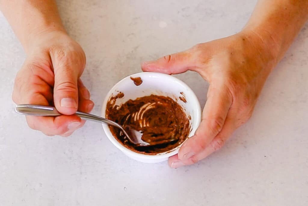 Stirring a bowl of lip balm and cinnamon to make homemade lip plumper.