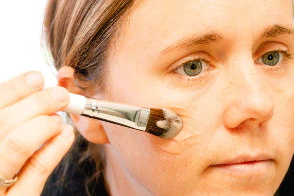 Using a foundation brush to apply a homemade liquid foundation to our cheek bone.