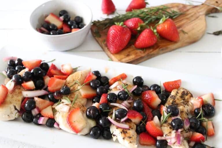 grilled chicken with berry salsa on white plate on white shiplap.