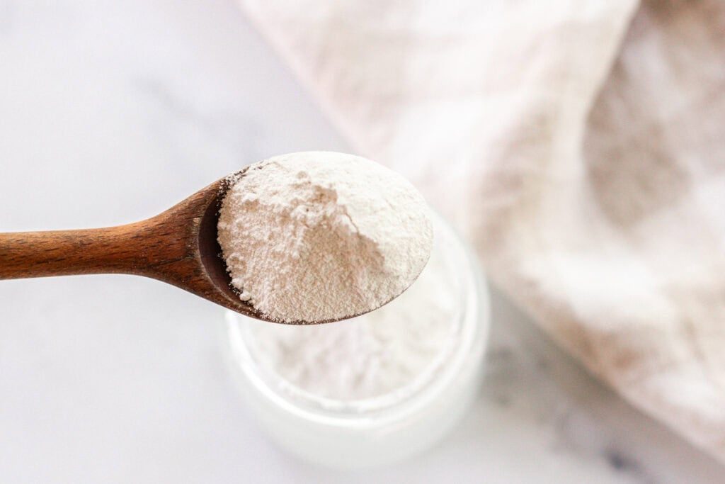 Using a spoon to add titanium dioxide and non-nano zinc oxide to a jar.