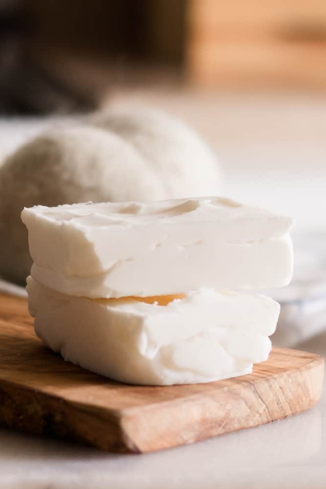 Two homemade laundry soap bars stacked up on wooden board.