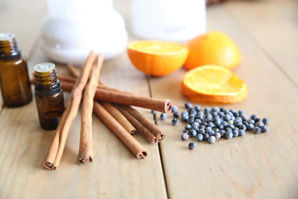 Cinnamon sticks, orange slices, and berries sitting on a wooden table with essential oils.