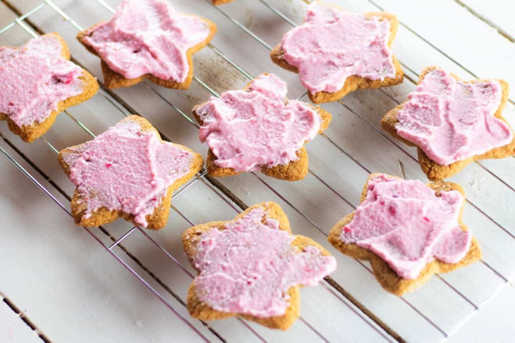 Paleo sugar cookies with pink frosting on a cooling rack.