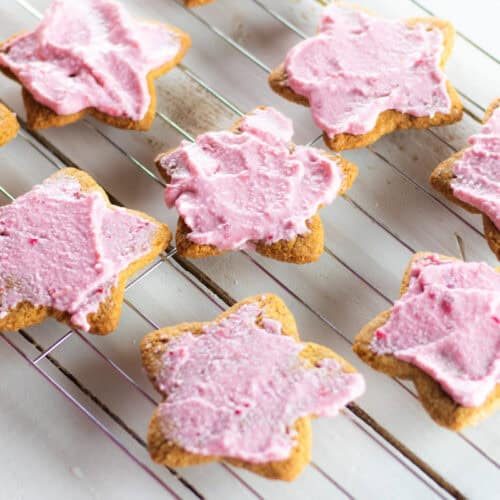 Paleo sugar cookies with pink frosting on a cooling rack.