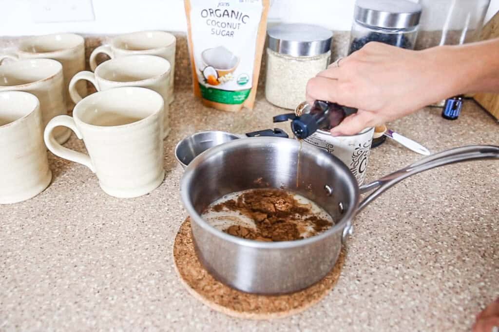 Dropping peppermint extract into a pot of paleo hot cocoa.