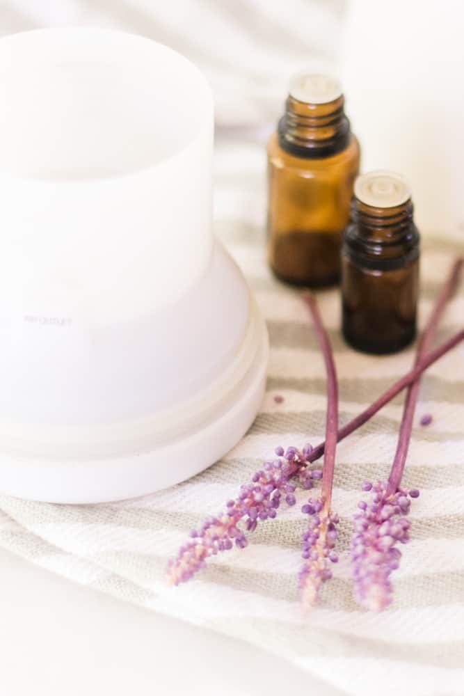 White diffuser with lavender sprigs around it and two amber colored essential oil bottles.