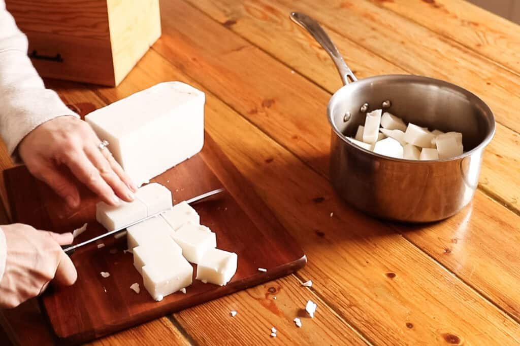 Chopping up a chunk of melt and pour soap base and putting it into a pot.