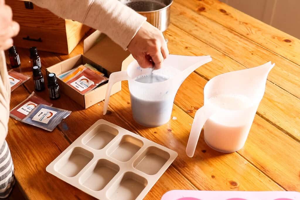 Stirring blue mica powder into one plastic pitcher of melted soap base.