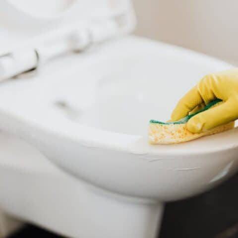 Scrubbing a toilet with foaming toilet cleaner and a sponge.