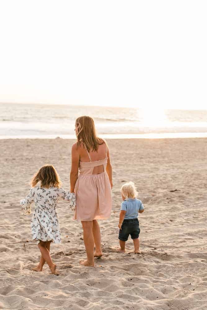 Women holding two kids hands while walking on the beach.