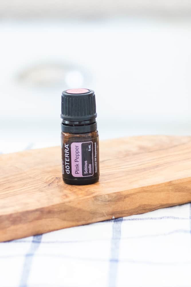 DoTERRA pink pepper essential oil bottle on wooden cutting board.
