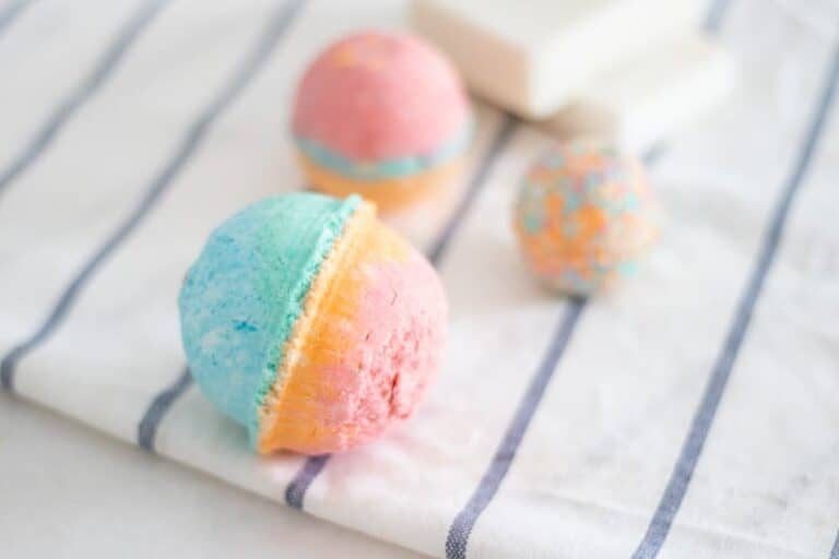 Three homemade rainbow colored bath bombs on white and blue towel.