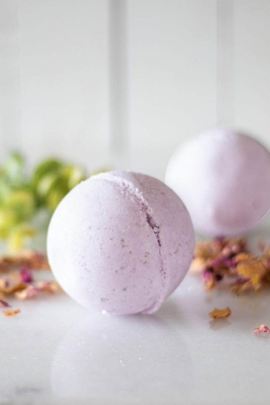 Two purple bath bombs with dried flowers and greenery.