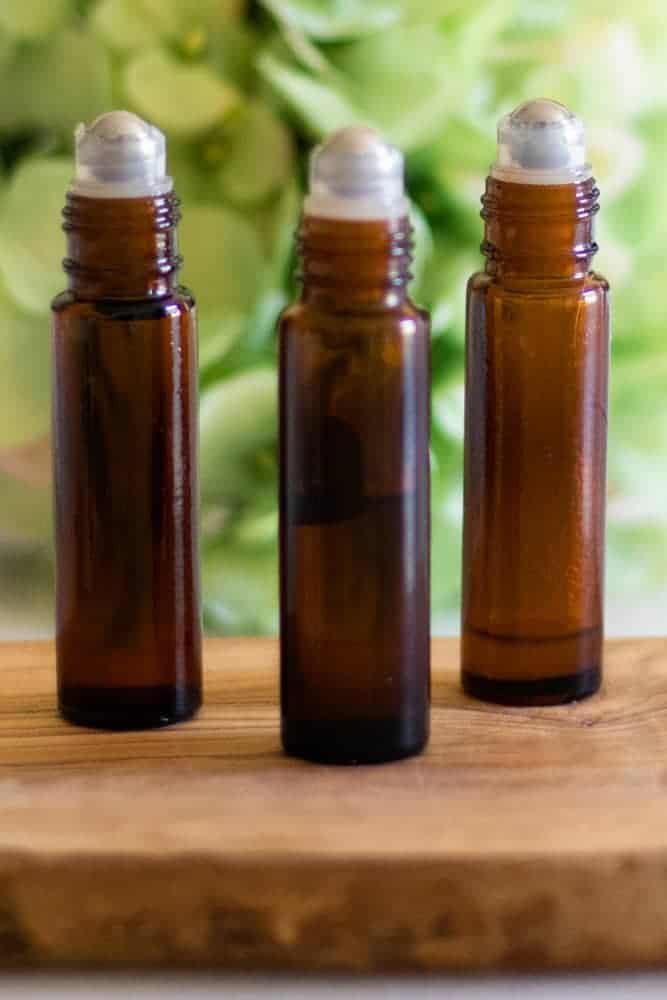 Three essential oil roller bottles standing on wooden board with green plant behind it.