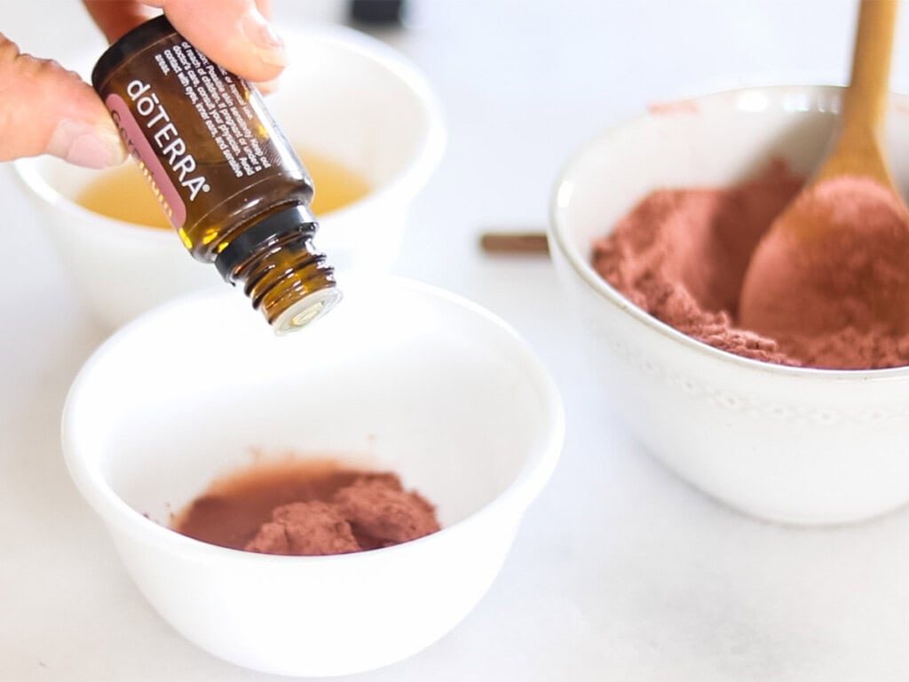 Dropping essential oil into a bowl of rose clay face mask.