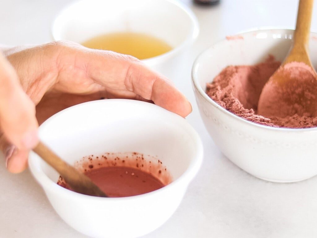 Stirring a rose clay face mask with a wooden spoon.