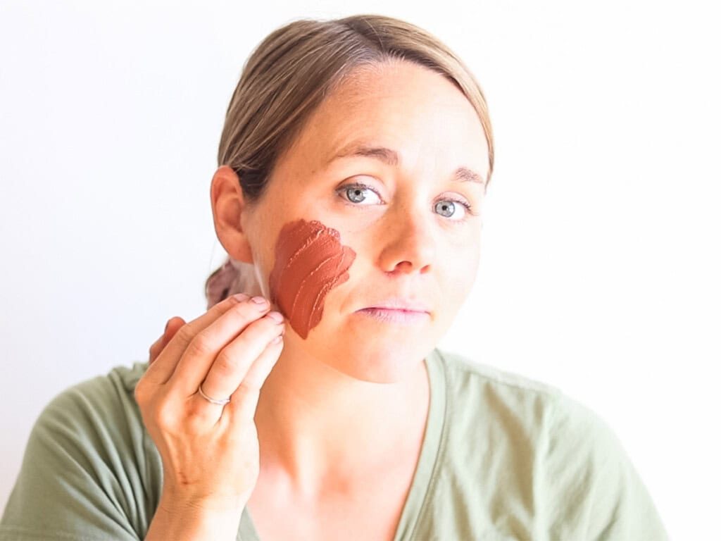 the studio spreading rose clay face mask onto her face.